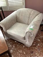 Photo showing the front and side view of a light-colored fabric upholstered armchair with rolled arms and cushioned backrest.