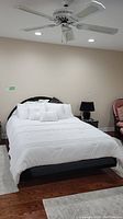 Full view of bed made up with white bedding showing laminated retro bedframe with curved mirrored headboard.