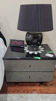 Front view of a bedside table showing black laminate top, mirrored drawer fronts, and objects on top.
