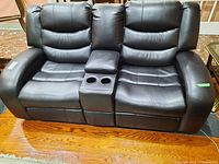 Front view of two-seat black leather recliner showing seats, stitching and central console