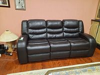 Front view of entire black leather sofa showing three seats and padded arms