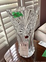 Front view of a clear crystal vase with jagged flared top, showing intricate fan and starburst cut glass pattern. Cristal d'Arques label and green sticker with number 12 are visible.