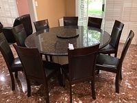Eight dark brown wood chairs with pleather seats and backs arranged around a round granite table