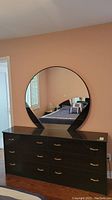 Front view of dark brown laminate dresser with six drawers and attached large round mirror.