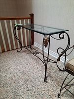 Side angle showing metal scrollwork and leaf accents on the legs and clear beveled glass top of hall table.