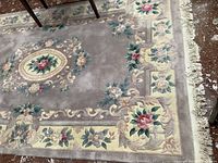 Close-up of floral pattern on wool area rug showing beige background with red and pink flowers with green leaves.