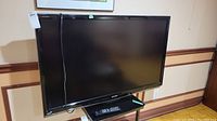 Front view of Sharp Aquos 52 inch TV showing screen and base stand with power cord hanging.