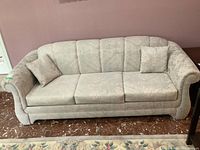 Front view of vintage upholstered three-seat sofa with two matching cushions in light beige patterned fabric.