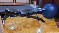Side view of black adjustable weight bench with blue exercise ball in background on wooden floor.