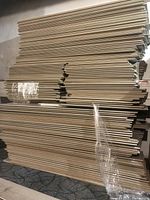Large stacked pile of beige-grey laminate flooring boards showing edges and multiple bundles