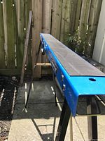 Side view of blue top edge and black metal legs of the folding sawhorse showing the brand plate and leg structure