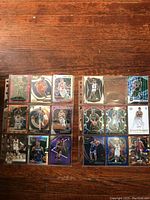 Photo of 16 sleeved basketball cards arranged in four rows of four on a wooden surface. Cards feature various players and holographic designs.