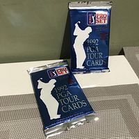 Photo of two sealed blue foil packs of 1992 Pro Set PGA Tour golf trading cards standing upright against a plain background.