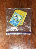 Photo showing a stack of original Pokemon cards with Totodile card on top inside a clear zippered bag on wood floor