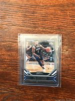 Close-up photo of Zion Williamson rookie basketball trading card in protective plastic sleeve laying on wood surface.