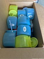Top view photo showing a box of multiple blue and lime green fish tank shaped plastic cups with lids and straws inside.