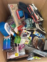 Photo showing assorted miscellaneous household items including 4-piece smoking thermometer in box, smartwatch covers in packaging, cleaning brush, Cooler-Brightz pack, snacks, and other small packaged items in a box.