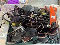 Photo showing a pile of brand new sunglasses with visible tags, various frame and lens styles and colors.