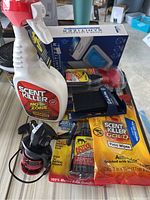 Photo showing multiple Scent Killer products including Zone spray bottle, Ants Field Wipes, Active Scent Repellent spray, a black and red fishing reel, and a phone sanitizer box in background.