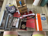 Photo showing all items in the lot including jewelry, accessories, a VHS tape, outdoor cleaner, LED lights, and inflatable cushion.