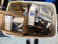 Overhead view of plastic tub containing mixed tools, hardware boxes, spray paint can, and manuals, showing the overall assortment of the lot.