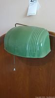 Green Art Deco style bed light mounted on a wooden headboard, showing front embossed design and ridged sides.