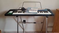 Casio CA-100 keyboard on metal adjustable stand with power adapter and instruction manual on top