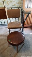 Vinyl chair with brown seat and backrest, chrome tubular legs next to a round brown material-covered stool with wooden legs.