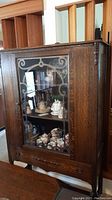 Front left angle view showing the glass door with etched decorative pattern and visible shelves displaying china items inside.