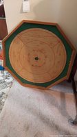 Full view of the octagonal wooden Crokinol board with scoring zones and green felt border leaning against the wall.