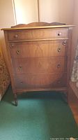 Front view of the tall boy dresser showing five drawers, decorative drawer pulls, wood veneer pattern, and curved top.