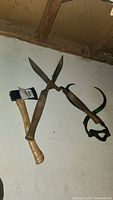 Photo showing hatchet with blue painted metal head alongside antique ice block hook and gardening shears hanging on wall.