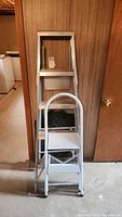 Photo showing the 4-step metal step ladder and the 5-foot folding ladder positioned together against a wooden wall.