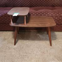 Front view of the two-tiered Mid-Century Modern end table showing the lower and upper surfaces with round tapered legs.