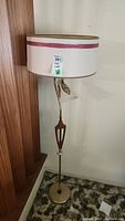 Full view of the floor lamp showing upper large white drum shade with red trim and brass-tone pole and base.