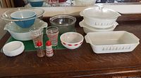 Full view of all items showing Pyrex and FireKing dishes, bowls, glasses, and salt and pepper shakers on a wooden surface.