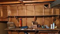 Photo showing the shelf with shoe shining kit supplies including polish tins, brushes, cloths, oil can, small tools, and green container.
