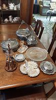 Photo showing the complete silverplate set arranged on wooden table, including pedestal dish, covered casserole, relish dish, butter dish, divided tray, small dishes, and wooden utensil holder with small forks/spoons.