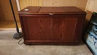 Front view of wooden storage chest showing three hinged top panels and vertical paneling on the front face.