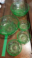 Overview photo of five uranium glass bowls showing two large and three small bowls arranged on a wooden surface, green strip placed beside bowls for scale.