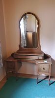 Front view of the wooden vanity desk with attached curved mirror, showing pull-out drawer and two side cabinets with doors.