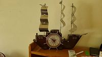 Full view of vintage Snider electric ship clock on wooden shelf, showing three metal wave-shaped sails and ship-themed design.