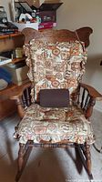 Front view of the wooden pressed back rocking chair with floral patterned cushion and lumbar pillow