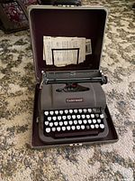 Front view of vintage Underwood typewriter inside the open brown carrying case with instruction sheets in lid.