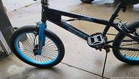 Side view of black Mongoose Crush bike with blue rims and fork showing frame, pedals and kickstand