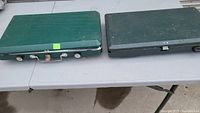 Two closed green Coleman camping stoves side by side on table