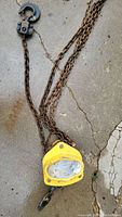 Photo of the yellow chain fall hoist and attached rusty chains on concrete floor.