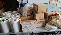 Large quantity of crochet thread in containers and boxes on a table, including packaging and bags.