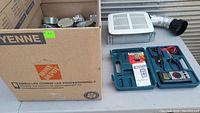 View of lot showing Mastercraft tester kit in blue plastic case next to boxed electrical items and a bathroom exhaust fan with duct attached.