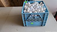 Blue plastic crate filled with white golf balls on a table